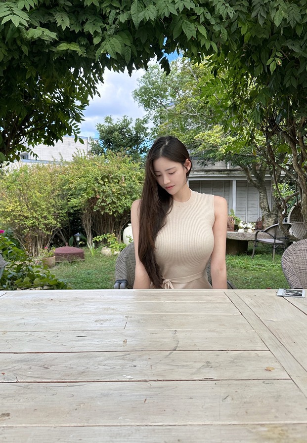 สาวเกาหลี jzx1xy ในชุดเดรสแขนกุดสีเบจนั่งที่โต๊ะไม้ในคาเฟ่ท่ามกลางสวนสีเขียว