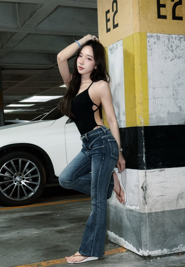 ดอนัทในบอดี้สูทสีดำกับยีนส์ขาม้ายืนพิงเสาในลานจอดรถ